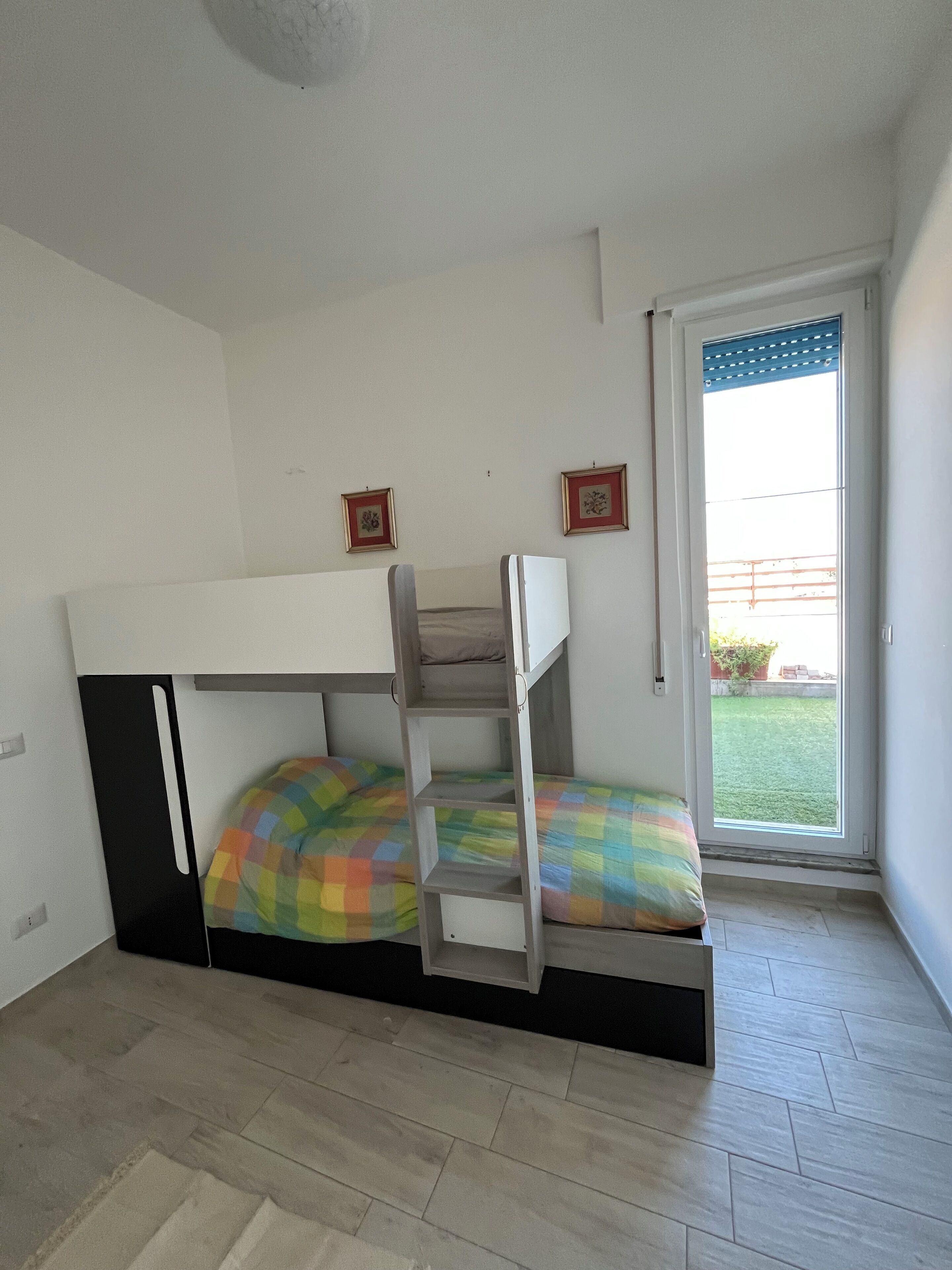 A room with a bunk bed, a ladder, and a sliding glass door leading to a balcony.