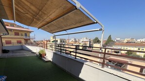 Una terraza en la azotea con césped artificial, barandilla de metal y un toldo grande.