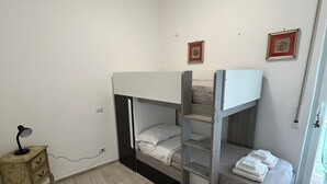 Habitación con literas, una mesita de noche pequeña y una lámpara, un cuadro en la pared y una ventana con vistas.