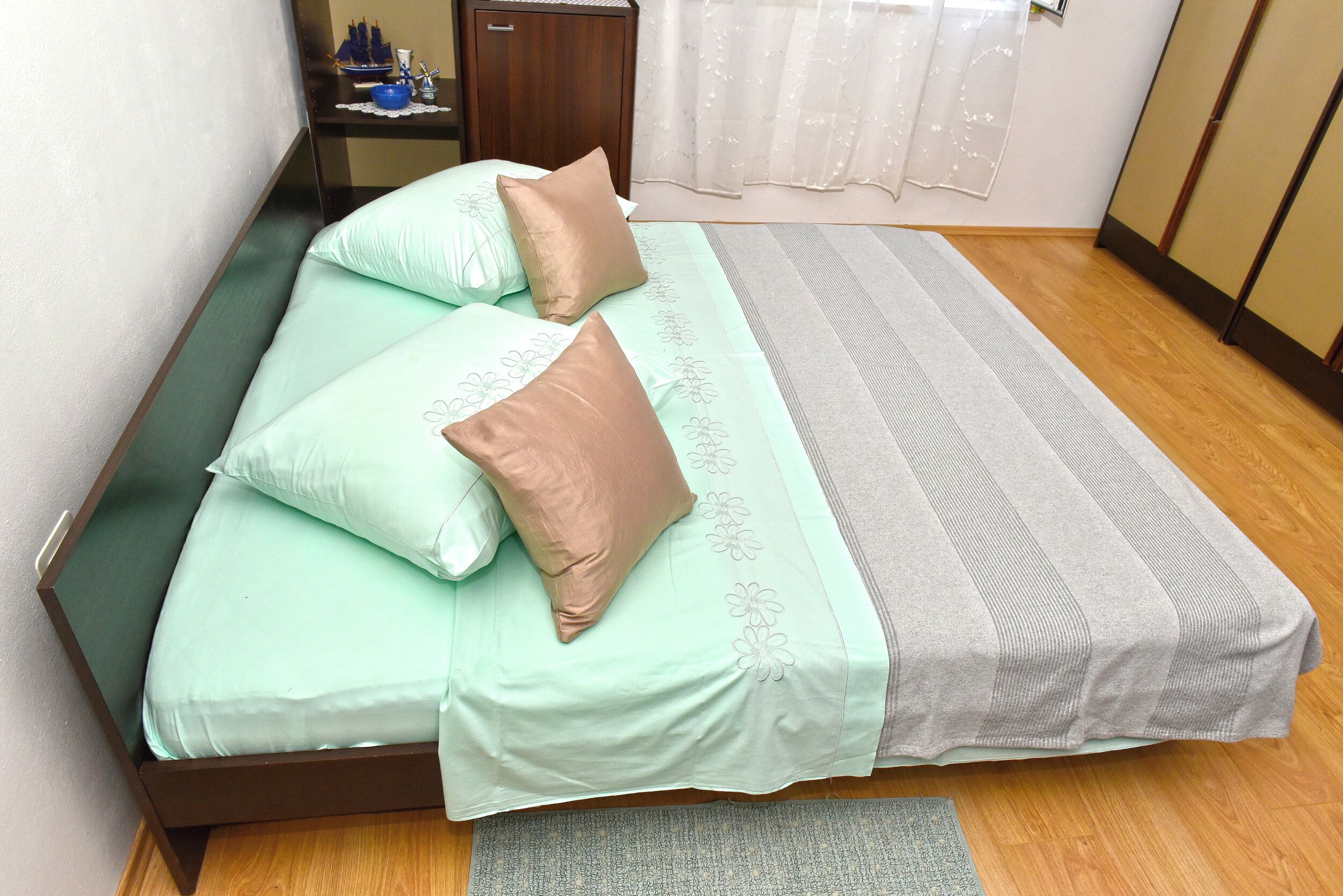 A neatly made bed with a green and white bedspread, two pillows, and a gray blanket.