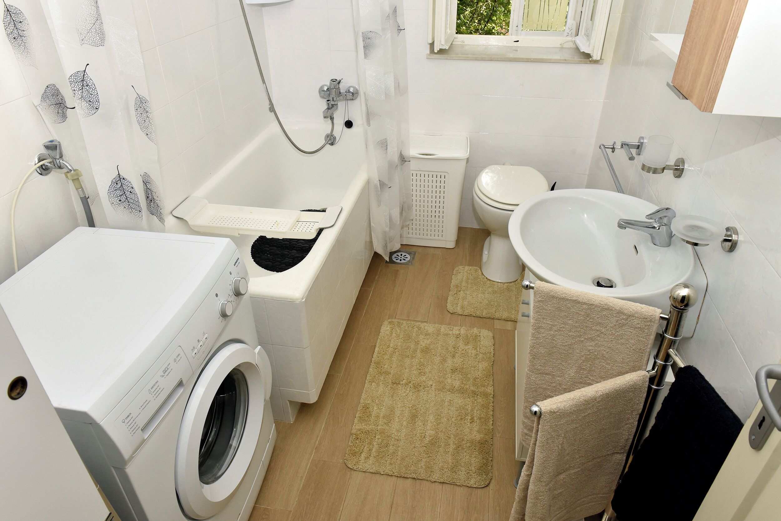 Ein kleines Badezimmer mit Waschmaschine, Badewanne, Toilette und Waschbecken.