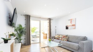 A modern living room with a grey sofa, a glass coffee table, and a flat-screen TV mounted on the wall. There are potted plants and a small table with a plant on it. - Home2Book Stylish Apt Fañabé, BBQ Terrace & Pool (Adeje)