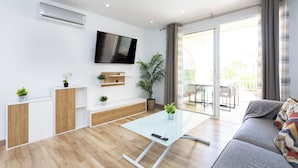 A modern living room with a flat-screen TV, a glass coffee table, a sofa, and a sliding glass door leading to an outdoor patio. - Home2Book Stylish Apt Fañabé, BBQ Terrace & Pool (Adeje)
