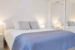 Ein ordentlich bezogenes Bett mit einer blauen Steude, weißen Kissen und einem Nachttisch mit einer Lampe.