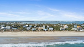 A coastal residential area with houses along the beach, a clear sky, and a view of the ocean.