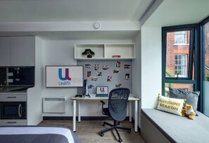A modern bedroom with a bed, a desk with a computer, and a window with a view of a brick building. - Student Only Bargate House (Southampton)