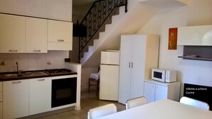 Une cuisine de taille réduite, avec des meubles blancs, une cuisinière, un four à micro-ondes et un réfrigérateur.