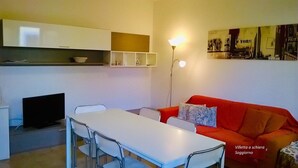Un espace de vie compact comprenant une table à manger, des chaises, un canapé rouge et un téléviseur.