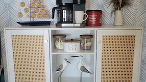 A white cabinet with rattan panels, a coffee maker, a mug, and decorative items including a bird sculpture and a vase with dried plants.