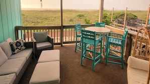 A covered outdoor seating area with a table and chairs, a sofa, and a view of the landscape.