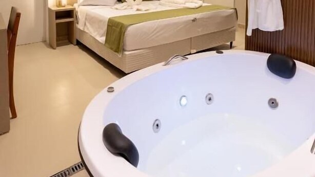 A modern hotel room with a large bed, a sitting area, and a hot tub. - Aira Hotel (Sobral)