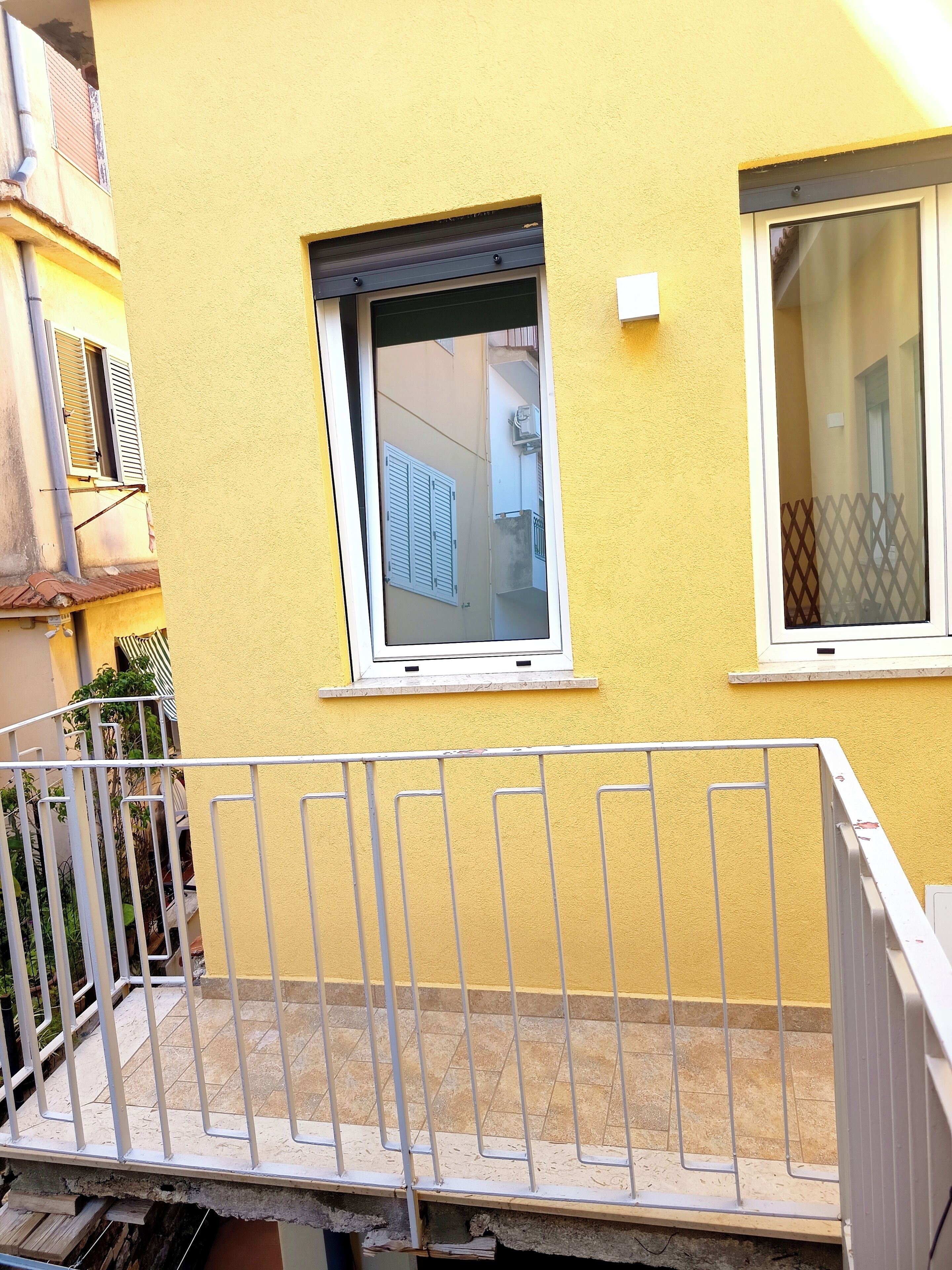 A yellow building with two windows, a metal railing, and a tiled floor.