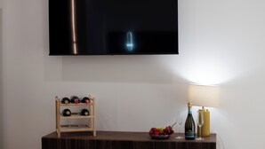 A flat-screen TV mounted on a wall, a wooden wine rack with bottles, a bowl of fruit, a bottle of wine, and a lamp on a wooden table. - Gold Leaf Sicily "Superior Triple Room" Taormina center (Taormina)