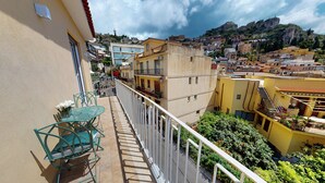 A balcony with a table and chairs, overlooking a cityscape with buildings and a hill. - Gold Leaf Sicily "Superior Triple Room" Taormina center (Taormina)