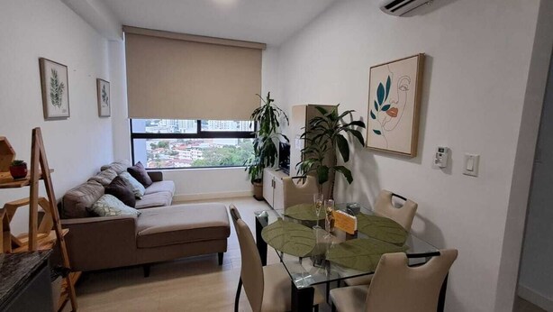 Ein modernes Wohnzimmer mit einer Couch, einem Glastisch und Blick auf die Stadt durch große Fenster.