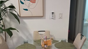 Ein Essbereich mit einem Glastisch, beigen Stühlen, einer Topfpflanze und einem gerahmten Kunstwerk an der Wand.