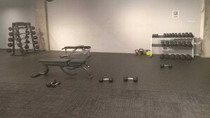 Ein Fitnessraum mit einer Bank, Kurzhanteln, Kettlebells und einem Squat-Gestell.
