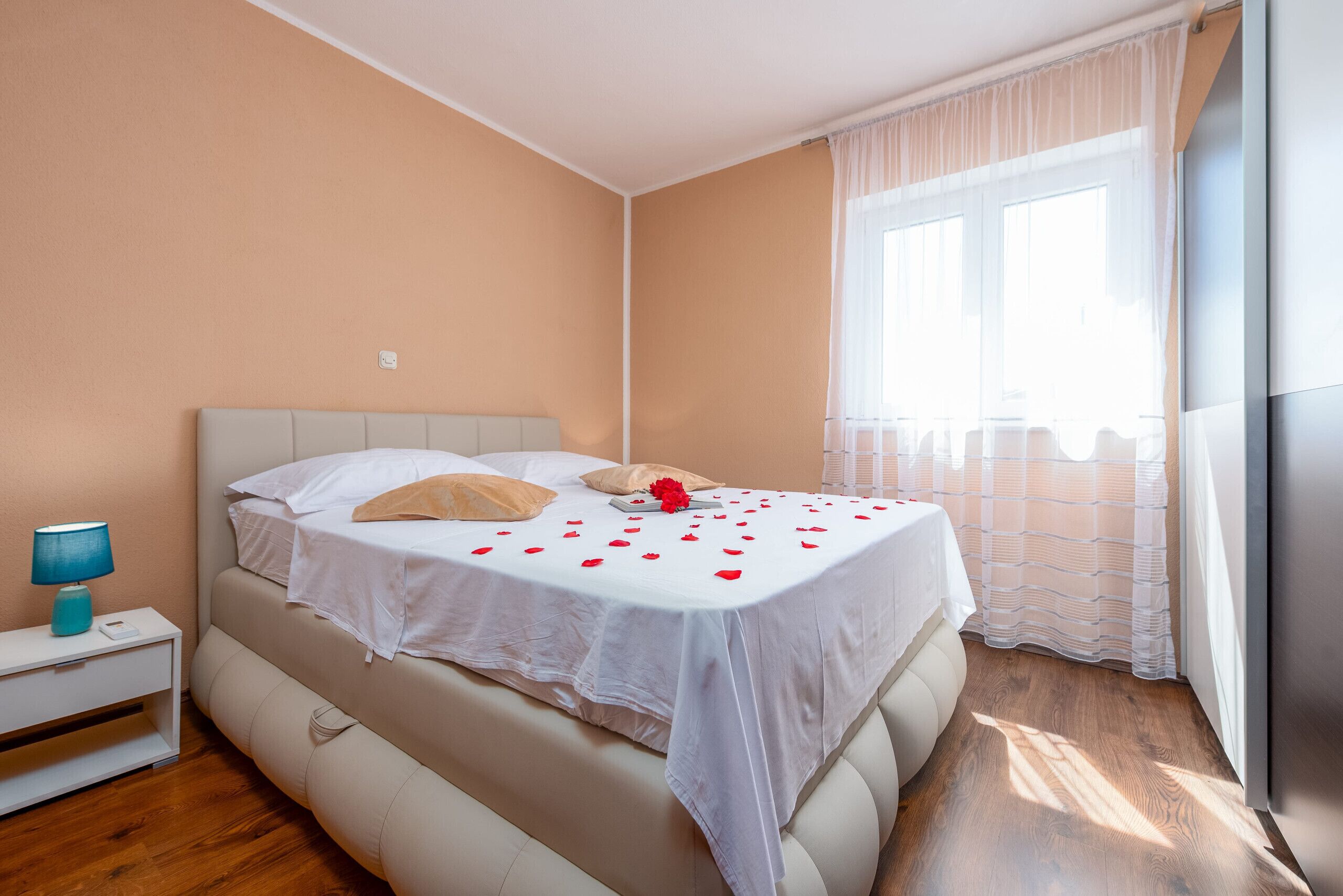 Ein Schlafzimmer mit einem Bett, einem Nachttisch und einem Fenster mit durchsichtigen Vorhängen.