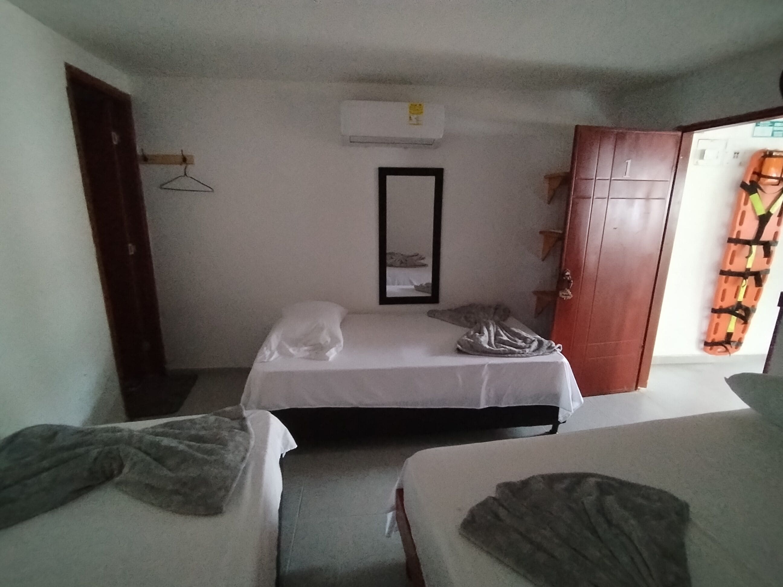 Une chambre avec deux lits, une armoire, un miroir et un appareil de climatisation.