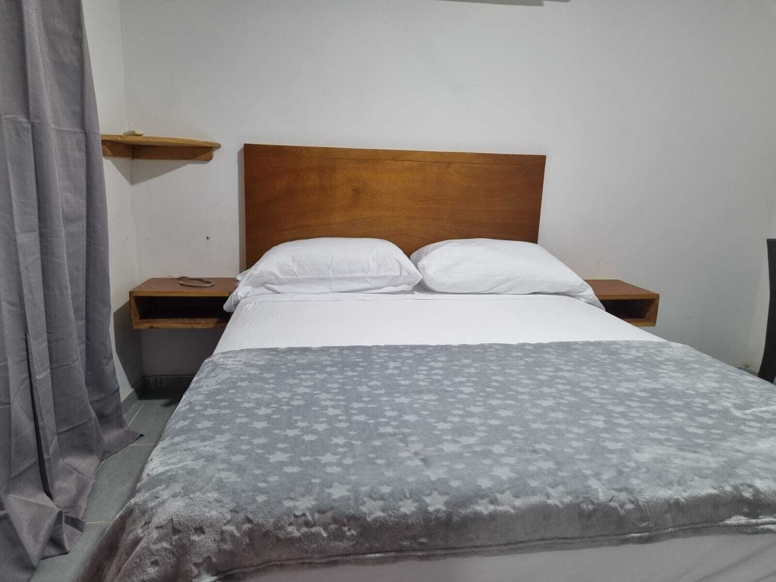Un letto rifatto con cura, con una coperta a motivi decorativi, una testiera in legno e due comodini con lampade.