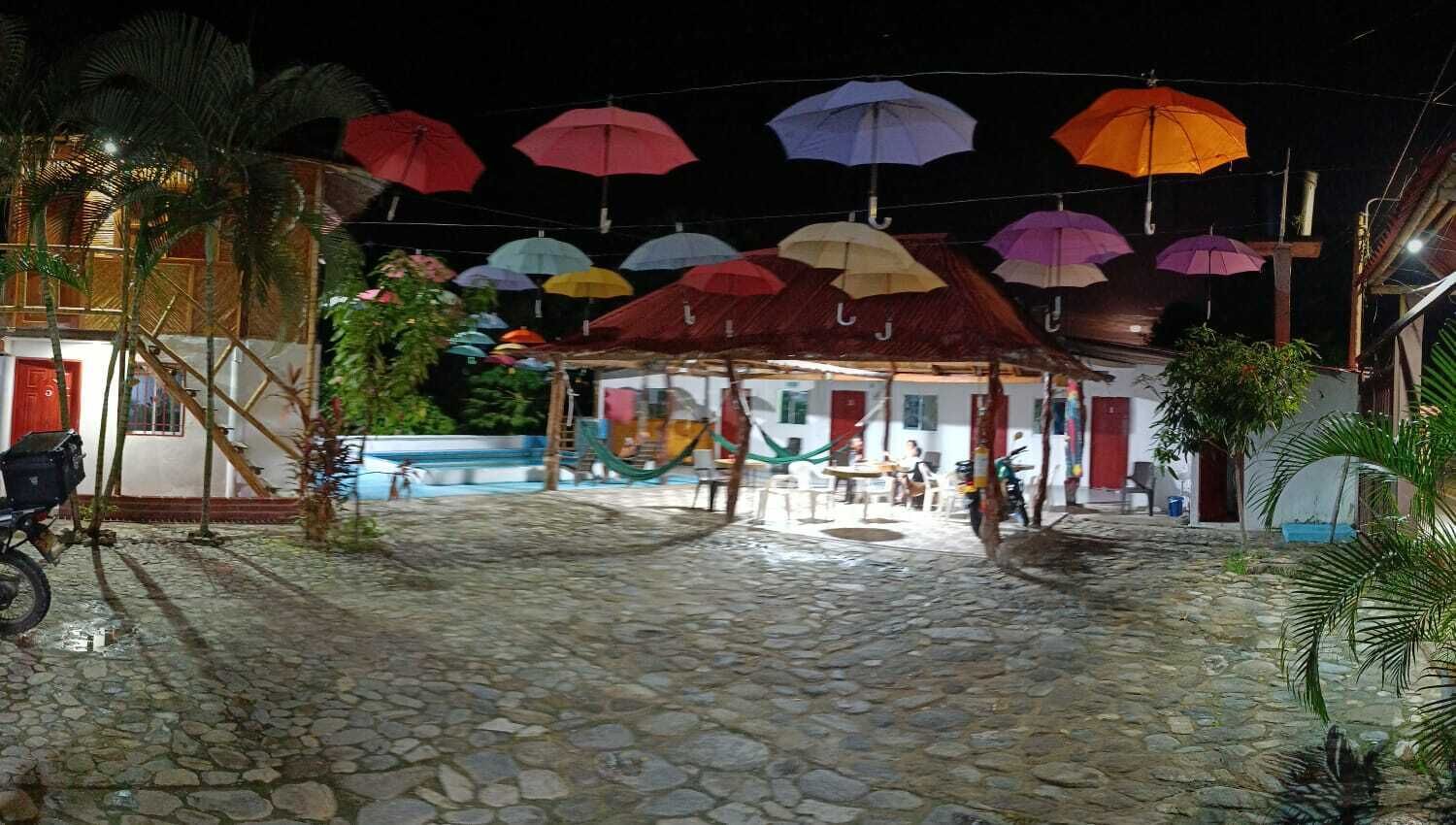 A cobblestone courtyard with a covered seating area, a pool, and a building with red doors.