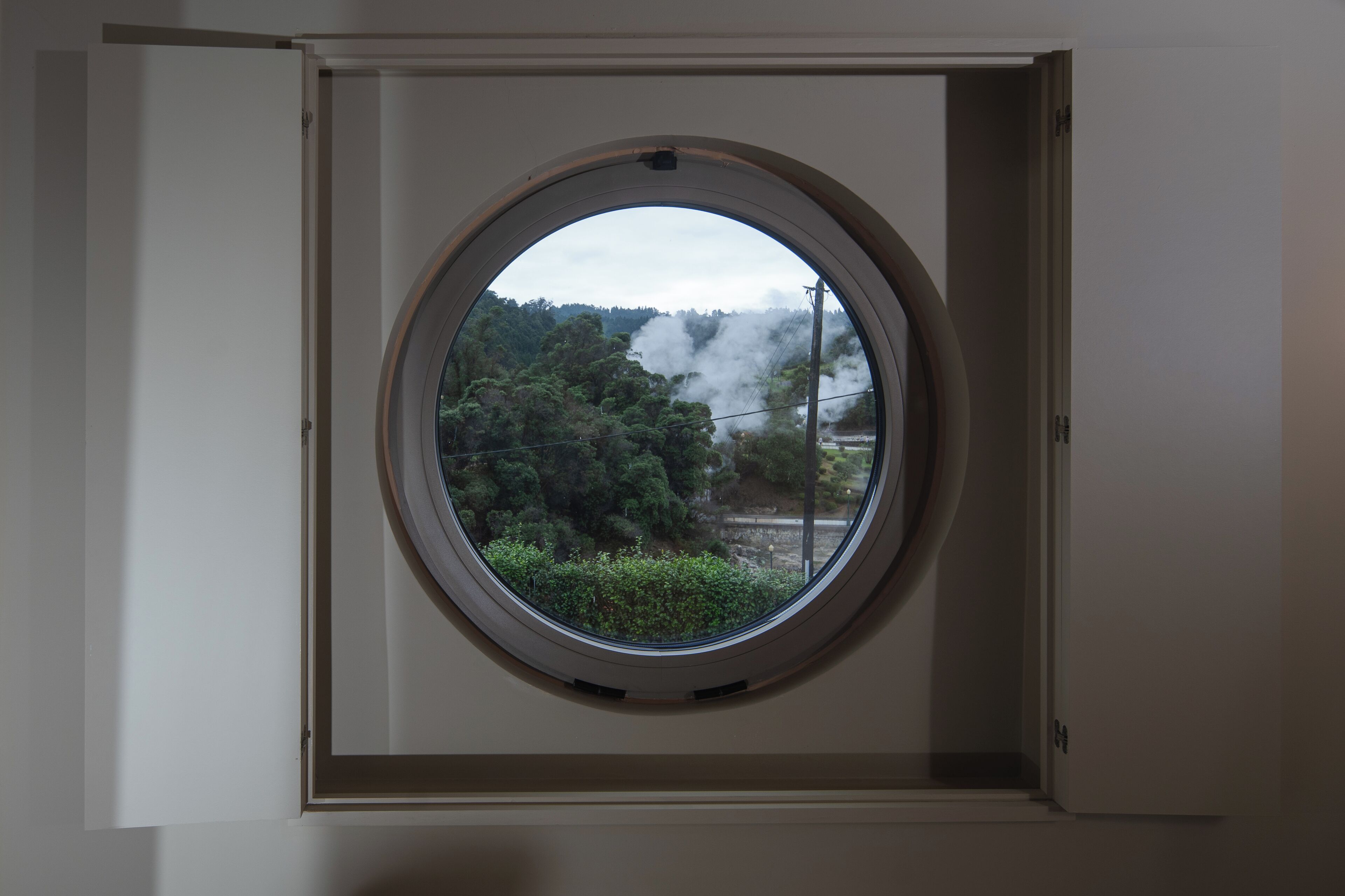 Una habitación con un ventanal circular que muestra árboles y un edificio con humo.