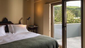 A bedroom with a bed, a bedside table with a lamp, and a view of a balcony with a scenic landscape. - Casa Nas Caldeiras (Povoacao)