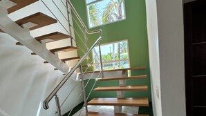 Eine moderne Treppe mit Holzboden und Metallgeländern, die zu einem Raum mit grünen Wänden und großen Fenstern führt.