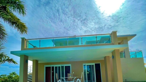 Ein modernes, zweistöckiges Haus mit Swimmingpool, großen Glasfenstern und einer Terrasse mit Gartenmöbeln.