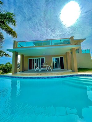 A modern two-story house with a swimming pool, large glass windows, and a patio with outdoor furniture. - Villages hills (Sosúa)
