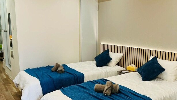 A hotel room with two beds, a wooden floor, a ceiling light, and an air conditioning unit.