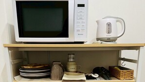 A compact kitchen area with a microwave, kettle, and storage shelves.