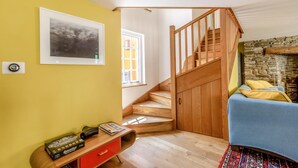 A room with a wooden staircase, a bed, a desk with a computer, and a stone fireplace.