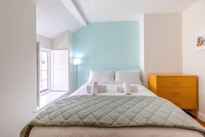 A bedroom with a bed, a bedside lamp, a dresser, and a window.