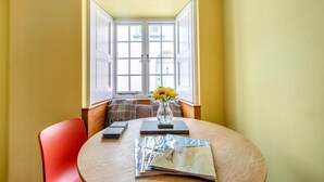 A dining area with a round table, a red chair, a vase with sunflowers, and a window with open shutters.