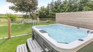 A hot tub with a wooden deck and a view of a playground in the background.