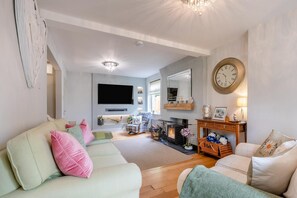 A living room with a fireplace, a television, and a large wall clock. - 4 Bed in Yarnscombe (oc-c32061) (Yarnscombe)
