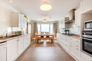 A modern kitchen with white cabinetry, a dining table, and a large window.