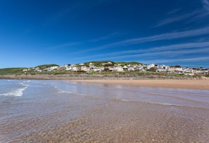 A coastal beach with clear skies, a sandy shore, and a row of houses on a hillside.