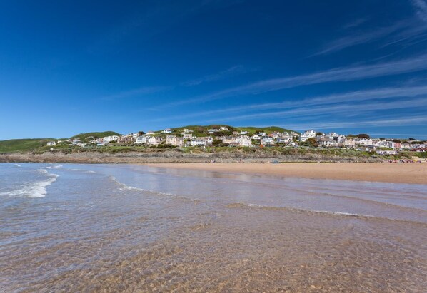 A coastal beach with clear skies, a sandy shore, and a row of houses on a hillside. - 4 Bed in Woolacombe (oc-w31785) (Woolacombe)