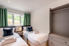 A twin room with two beds, a nightstand, a dresser, and a window with curtains.