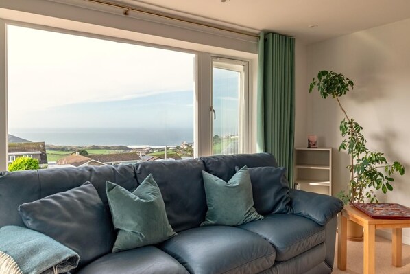 A living room with a leather sofa, a wooden side table, a potted plant, and a view of the sea.