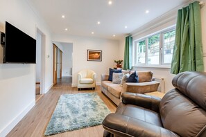 A modern living room with a sofa, armchair, and a flat-screen TV mounted on the wall. - 4 Bed in Woolacombe (oc-w31785) (Woolacombe)