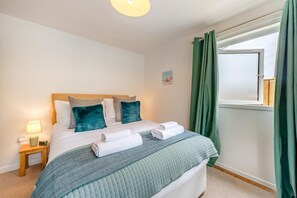 Una cama bien hecha con almohadas, una lámpara de noche y una ventana con cortinas.