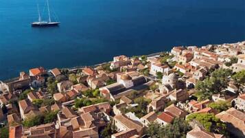 A coastal town with tightly packed buildings, a sailboat in the water, and a hilly backdrop.