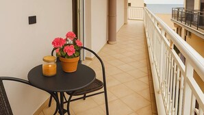 A balcony with a table and chairs, a potted plant, and a view of the sea.