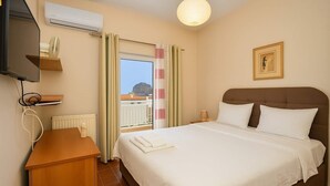 A hotel room with a bed, a desk, an air conditioning unit, a window with curtains, and a framed picture on the wall. - Cosmo Room 2 | Seaside Retreat | Monemvasia Castle (Monemvasia)
