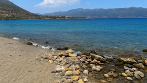 A rocky shoreline with clear blue water, a distant mountain range, and a person kayaking. - Cosmo Room 2 | Seaside Retreat | Monemvasia Castle (Monemvasia)
