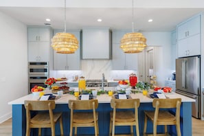 A modern kitchen with blue cabinets, stainless steel appliances, and a central island with chairs.
