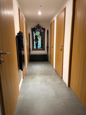 Un couloir bordé de portes en bois de part et d’autre, avec un sol carrelé et un miroir doté d’un cadre décoratif.